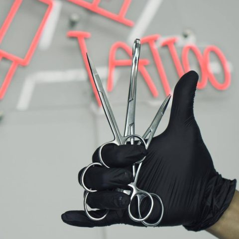 Gloved tattoo artist hand under the studio neon sign